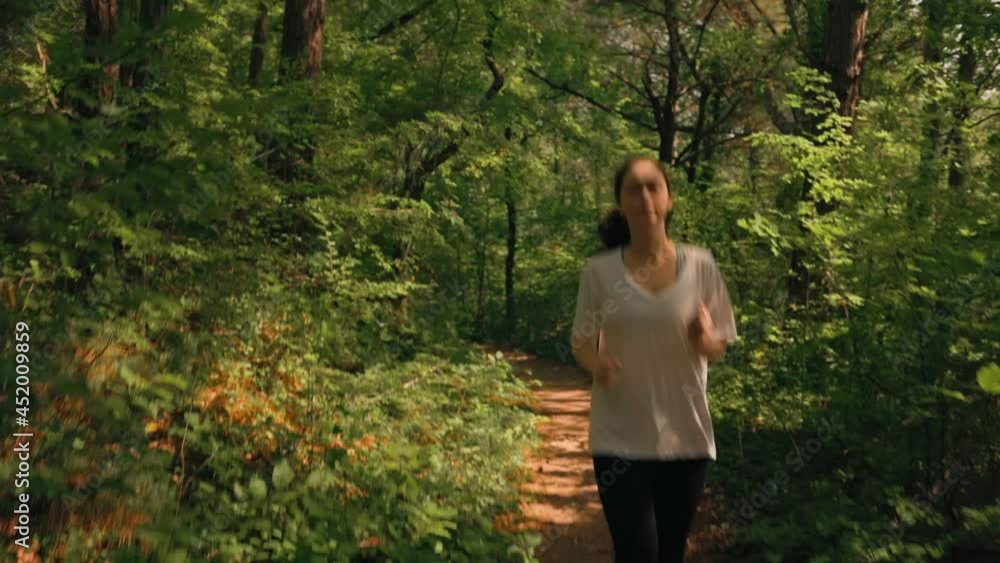 A young woman in sports clothes is jogging in the morning summer forest. Dolly and jib shot. Real time. The concept of a healthy lifestyle. A young woman in sports clothes is jogging in the morning summer forest. Dolly and jib shot. Real time. The concept of a healthy lifestyle.