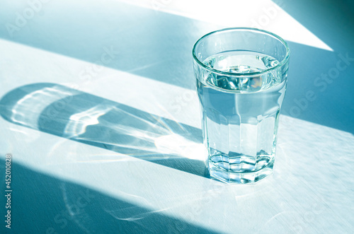A glass with clean clear water and sharp shadows stands on a white table