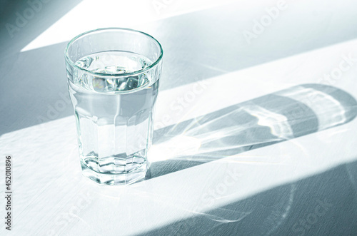 A glass with clean clear water and sharp shadows stands on a white table