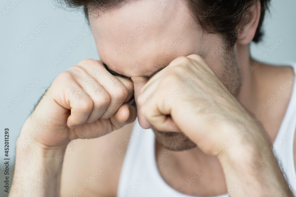 young man rubbing eyes with fists in morning