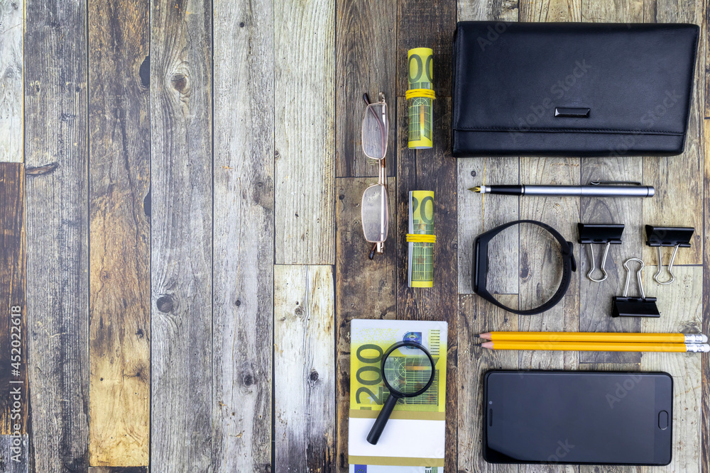 Office financial flat lay still life with 200 euro bills, magnifying glass, purse, smartphone and stationery over a grey wood background with copyspace Office financial flat lay still life with 200 euro bills, magnifying glass, purse, smartphone and stationery over a grey wood background with copyspace