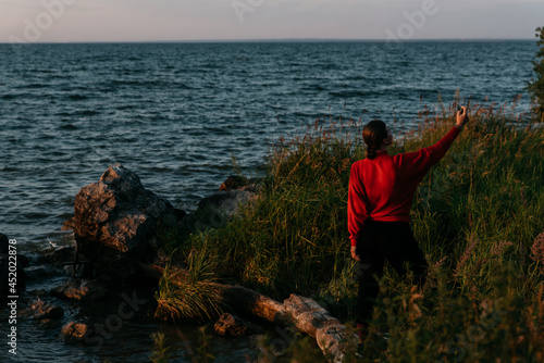 Photo  of a Summer Camping Activity. Travel location of popular tourist outdoor. View of beautiful Sea Landscape and Woman make selfie. Vacation by the lake in a camp with a bonfire and tent