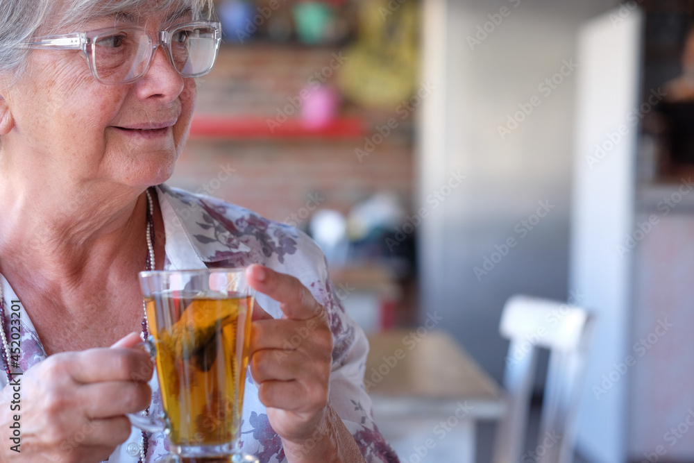 Portrait of beautiful elderly woman in coffee shop, enjoying herbal tea. Senior gray-haired people