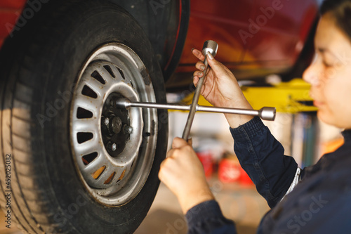 Mixed race female car mechanic wearing overalls, unbolting wheel of car photo