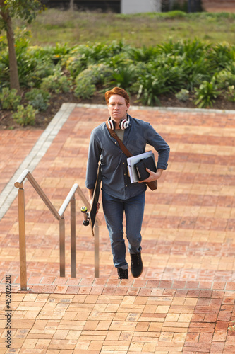 Serious caucasian male business creative walking upstairs holding notebooks and skateboard photo