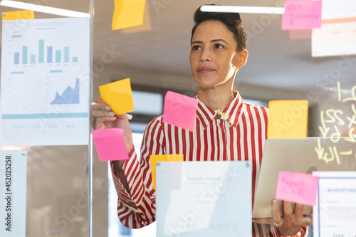 Serious caucasian female business creative brainstorming and writing memo notes on glass wall photo