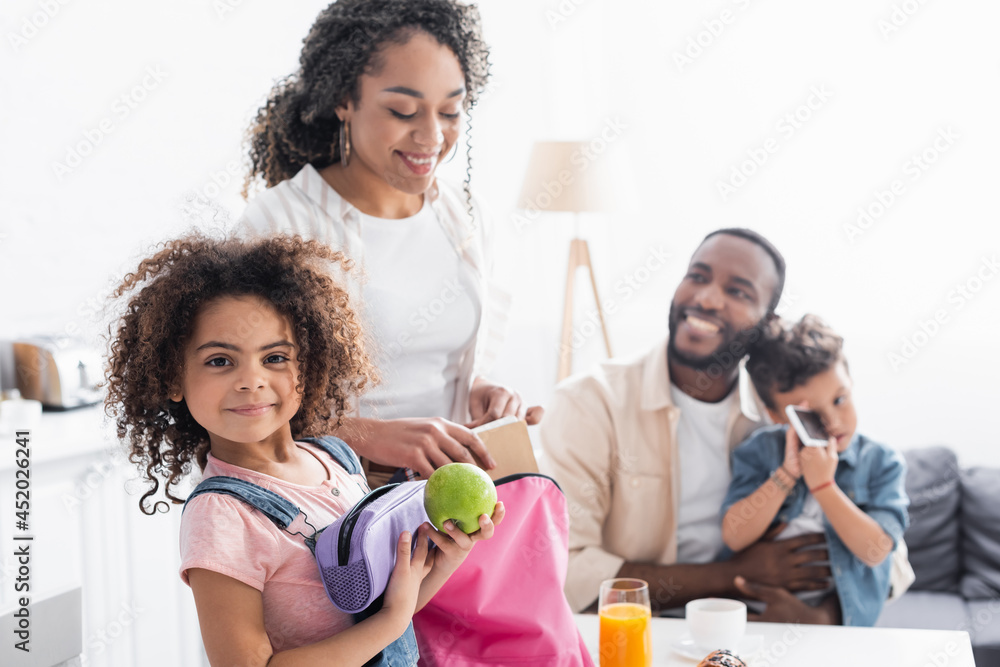 african american girl holding apple and pencil case near mother packing her backpack african american girl holding apple and pencil case near mother packing her backpack