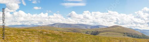Panoramic view of the mountain range. Cloudy sky and green tunra. Cloud shadows on mountains covered with dwarf birch and mosses