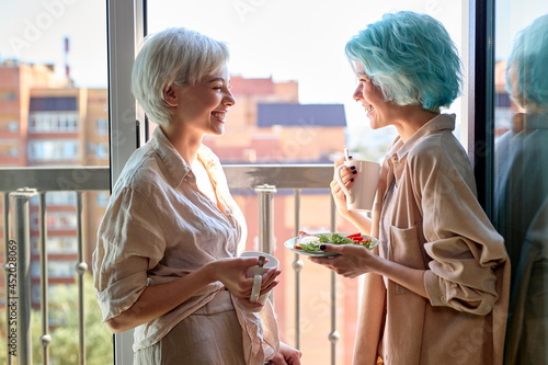 Side View Portrait Of Two Positive Caucasian Ladies Lgbt Couple Having Meal, Drinking Coffee On Balcony, Having Talk, Breakfast Time At Home, Weekends. People Lifestyle Concnept. Copy Space photo