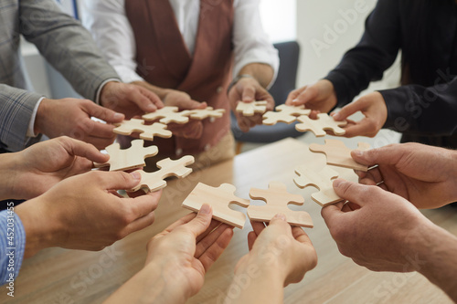 Team of business people joining pieces of jigsaw puzzle, closeup shot of hands holding jigsaw parts in circle. Group of entrepreneurs forming coalition or alliance. Cooperation and teamwork concept