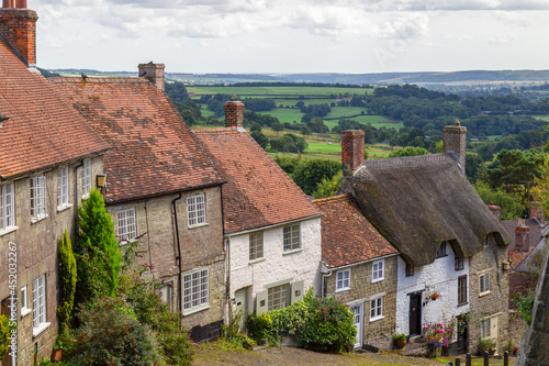 Old English houses with red roof tiles and thatched roofs and with green hills in the background (Golden hill) in the picturesque village of Shaftesbury, Dorset, England. photo