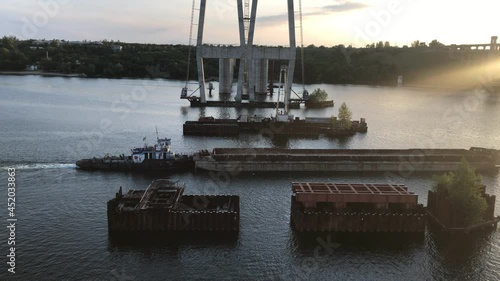 a large cargo barge without cargo passes along a wide river near the construction of bridges in the evening at sunset