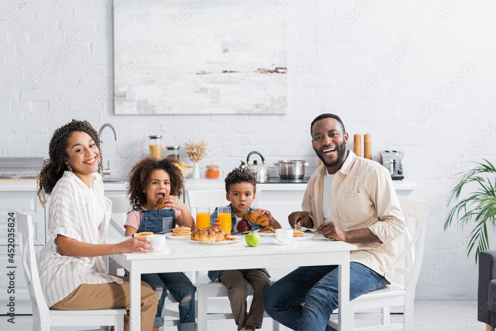Fototapeta premium happy african american couple smiling at camera during breakfast in kitchen