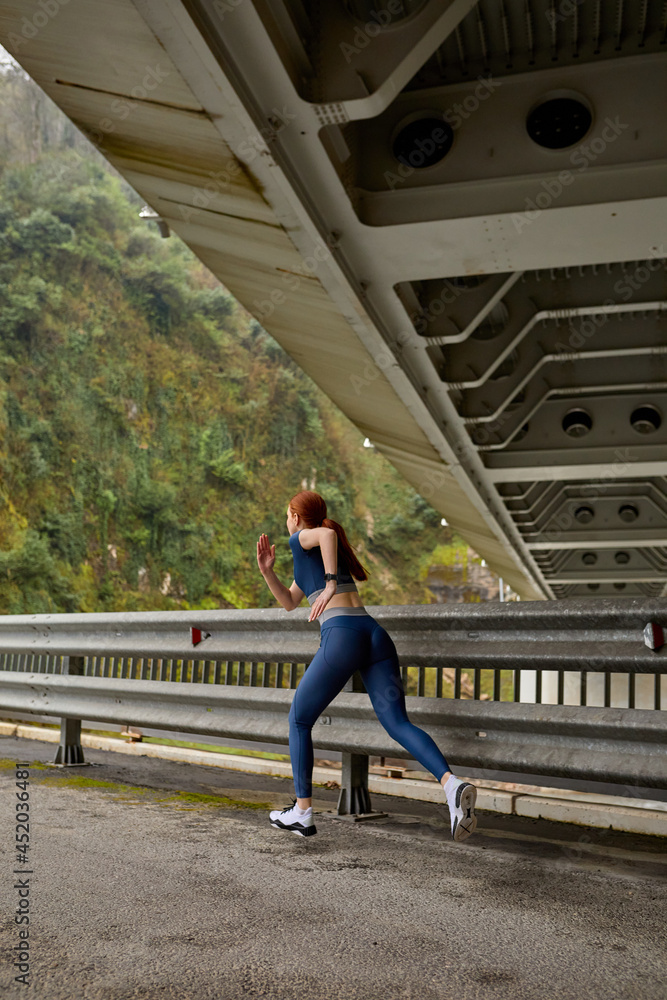 Young woman running jogging fast outdoors. Female athlete exercising on modern bridge. Side view on strong active vigorous lady in blue sportswear running forward, copy space. sport concept