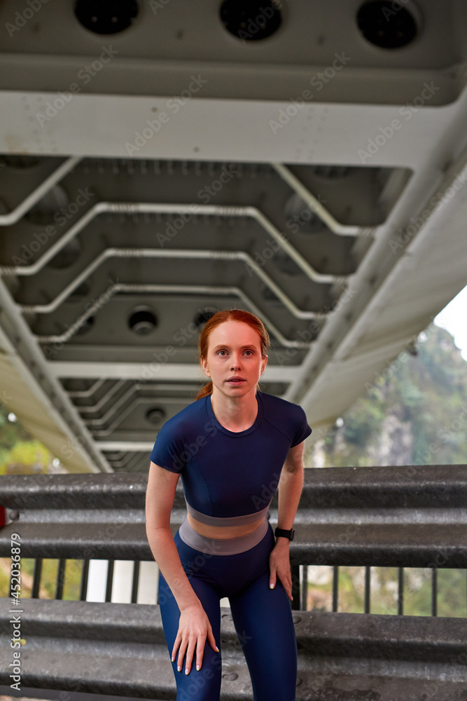 Serious Confident Runner Woman Is Getting Ready To Run, Preparing, Redhead Lady Is Looking Forward, Concentrated and Focused, In Modern Blue Stylish Sportswear. Portrait. Copy Space, People Lifestyle Serious Confident Runner Woman Is Getting Ready To Run, Preparing, Redhead Lady Is Looking Forward, Concentrated and Focused, In Modern Blue Stylish Sportswear. Portrait. Copy Space, People Lifestyle