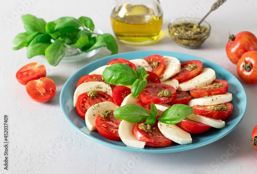 Italian caprese salad with sliced tomatoes, mozzarella cheese, basil and olive oil on a blue plate on light background.