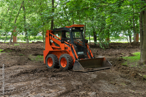 Skid steer loader clearing the site in public park moving soil and performing landscaping works for the territory improvement.