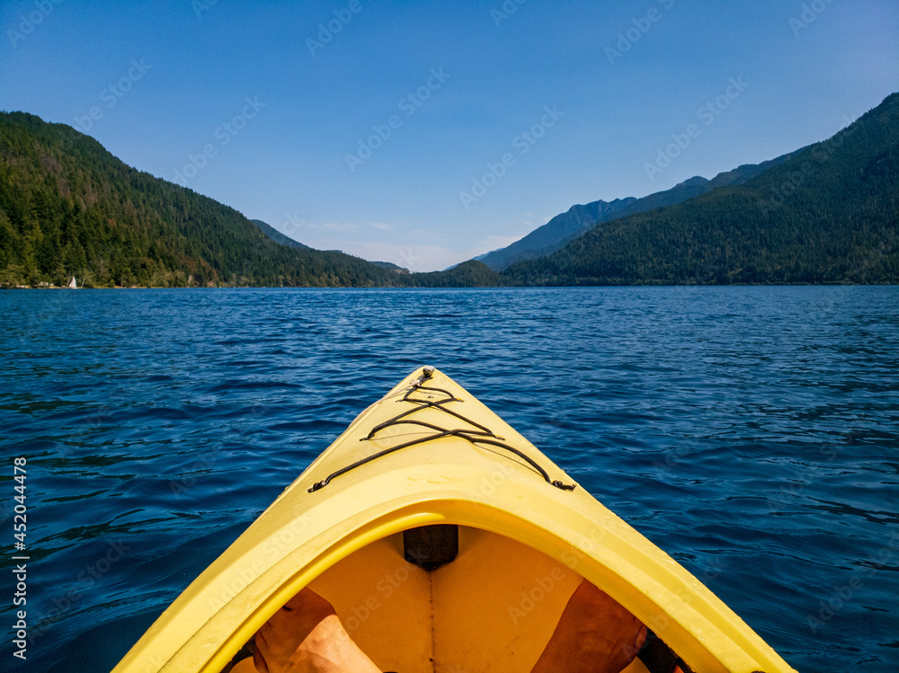 The tip of a yellow kayak on a blue water lake surrounded by hills