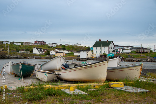 The small fishing community of Twillingate, Newfoundland, with small white fishing boats on a wooden slipway in the harbour with vintage wooden buildings and homes in the background. 