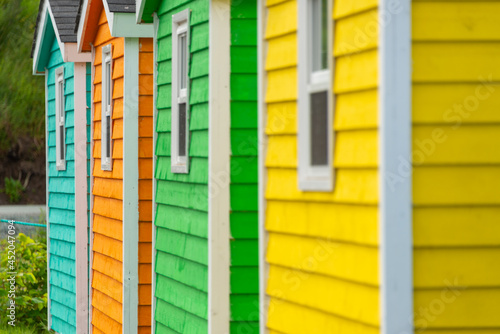 The exterior of a bright orange and green narrow wooden horizontal clapboard wall of a house with one vinyl window. The trim on the glass panes is white in color. 