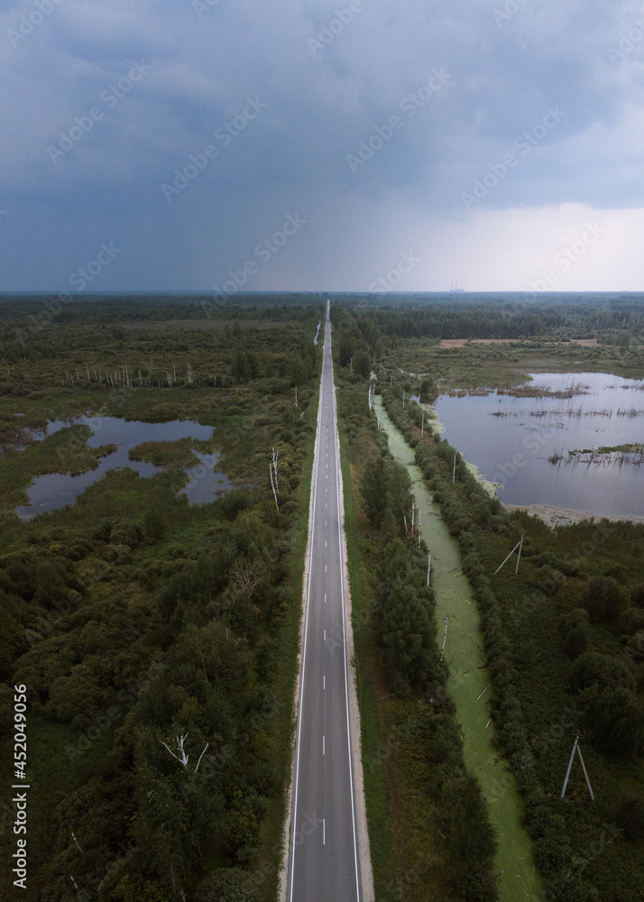 A road through the swampy area with the storm clouds on the background