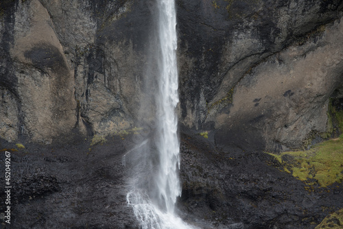 dünner hoher Wasserfall vor dunklen Felsen