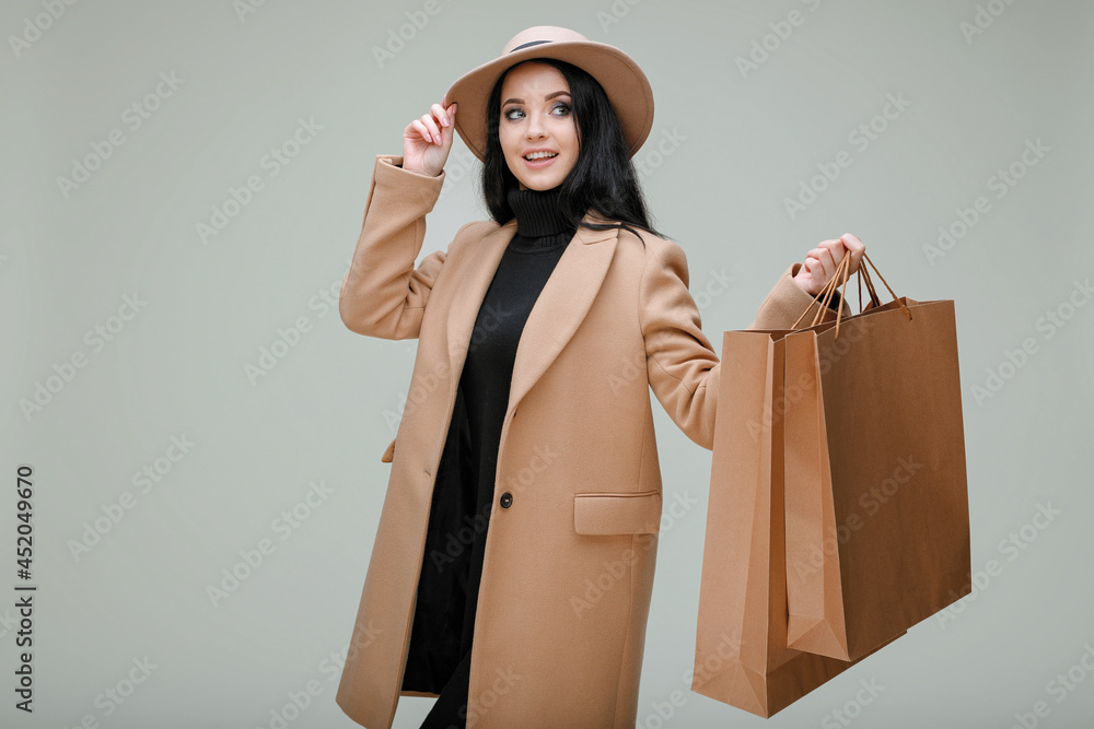 Φωτογραφία Portrait of charming lady in beige classic coat and hat with shopping bags in hands on gray background