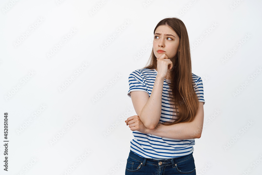 Young woman pondering, looking left and thinking, making choice, standing over white background Young woman pondering, looking left and thinking, making choice, standing over white background