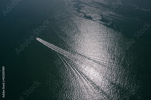Aerial shot of a single isolated boat in the ocean creating waves behind it.