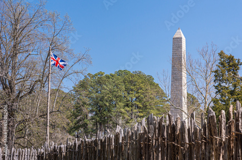 Jamestowne, VA, USA - April 1, 2013: Historic site. Tencentennial obelisk monument seen over defense wall of fort against blue sky. Some green foliage and British flag. photo