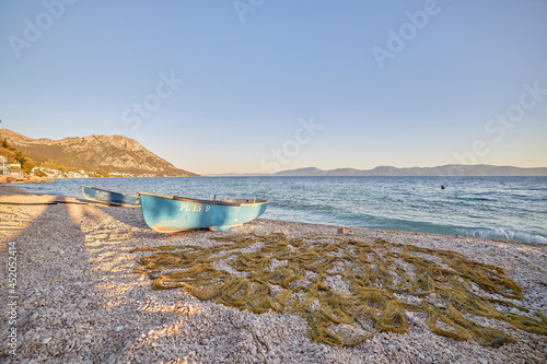 Fototapeta Naklejka Na Ścianę i Meble -  Blue fishing boat on an empty beach during sunset time in Gradac, Croatia