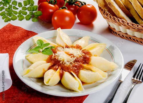 Murais de parede Conchiglione, massa típica da cozinha italiana, ao molho de tomate com queijo parmesão com cesta de pão italiano na mesa decorada