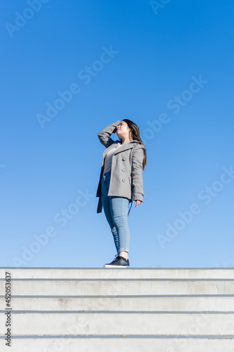 young hispanic latin woman at the top of the stairs successful. blue sky background. vertical photo with copy space