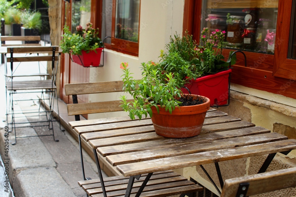 Beautiful interior of Paris cafe with summer terrace and tables with house plants in the European street, French lifestyle in Europe with authentic stylish design. Empty bistro with holiday ambiance.