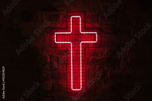 Foto Glowing red neon cross hangs on the wall behind the bars in the dark