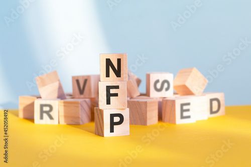 wooden cubes with letters NFP arranged in a vertical pyramid, yellow background