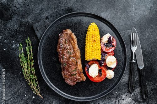 Roasted P beef steaks Striploin or New York on a plate with garnish. Black background. Top view