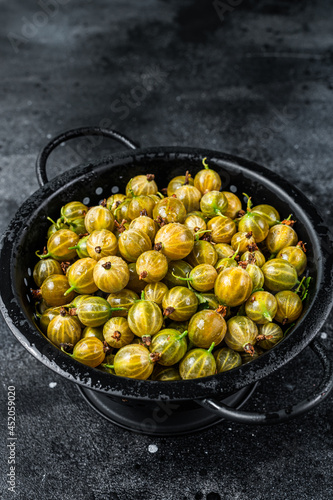 Fresh green gooseberries in a colander. Black background. Top view