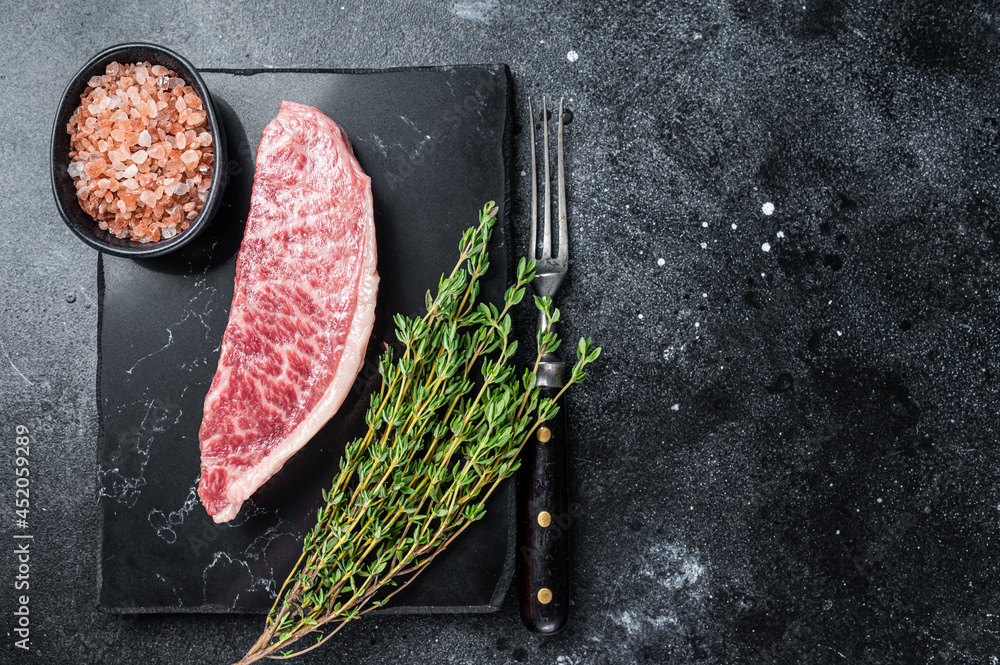 Wagyu raw sirloin steak, kobe beef meat on marble board. Black background. Top view. Copy space - obrazy, fototapety, plakaty 