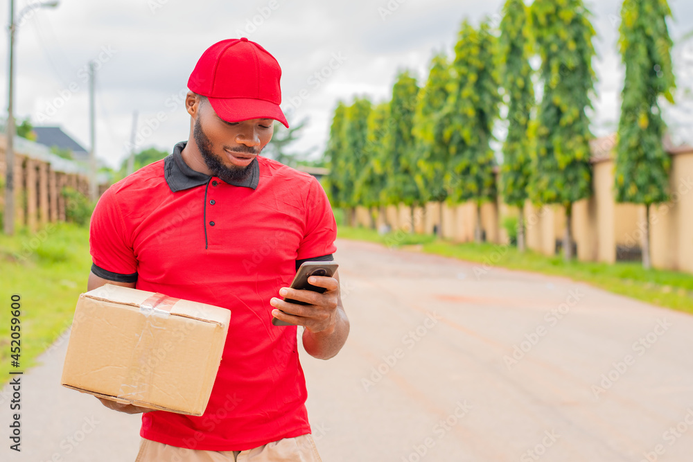 african delivery worker checking his phone while carrying a box african delivery worker checking his phone while carrying a box