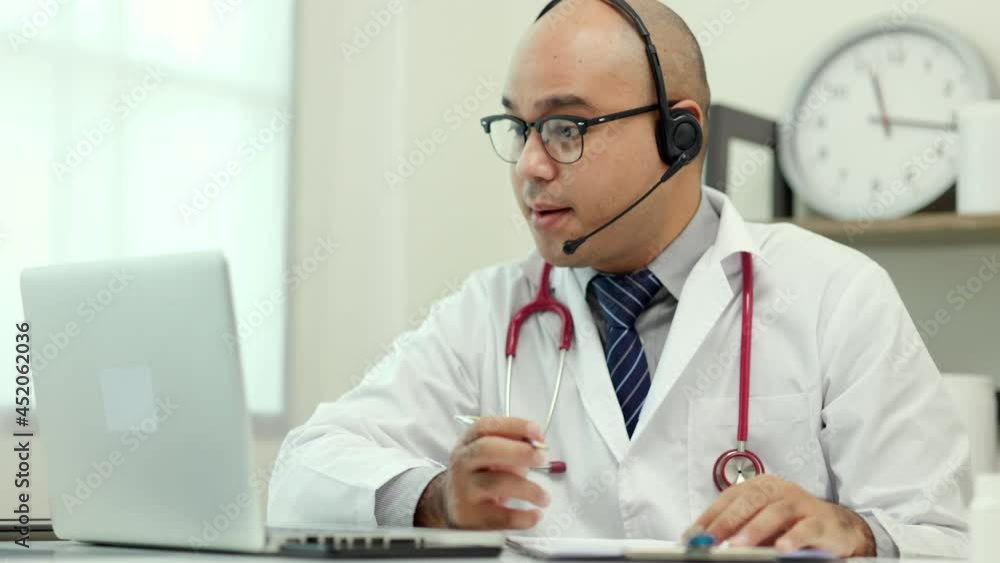 Doctor talks to patient via online video conferencing looking at laptop screen. Explain about taking medications to treat illnesses and note the report.
