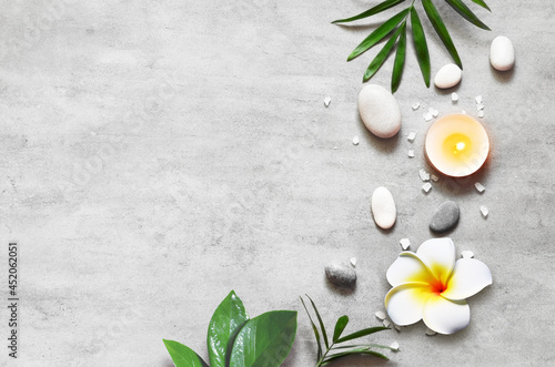 Spa concept on stone background, palm leaves, flower plumeria, candle and zen, grey stones, top view.