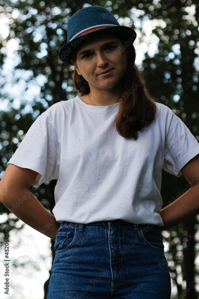 Defocus close-up portrait of a sad young woman with brown hair wearing a hat outdoors. Green nature background. Looking at camera. Women standing at dark park. Vertical. Out of focus Defocus close-up portrait of a sad young woman with brown hair wearing a hat outdoors. Green nature background. Looking at camera. Women standing at dark park. Vertical. Out of focus