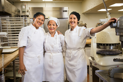 Portrait of three smiling female bakers in kitchen surrounded by culinary appliances.  photo