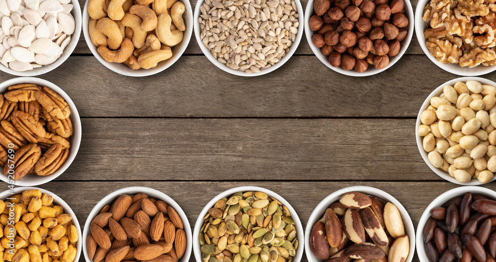 Assorted nuts and seeds in bowls over wooden table with copy space