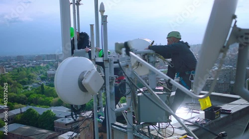 Workers servicing cellular antenna in front of city . Contractors working on a telecommunications mast at height .  Telecommunication technician working on top of cellular antenna. The cell tower