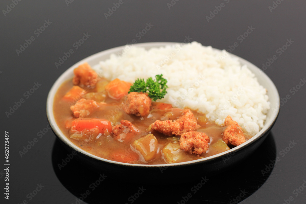 Japanese or Korean Curry with Rice - Japanese Food Style. Served on Ceramic Plate Isolated Black Table  with Potato , Crispy Chicken Popcorn, and Carrot Dice, Copy Space for Text