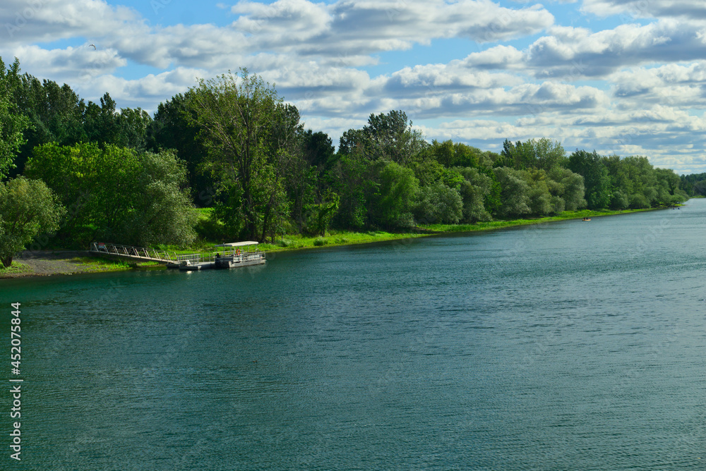 A boat in the river in between the islands of Boucherville national park in Lawrence (Laurent) River, Montreal, QC on a cloudy summer day. The trees and grass on the river banks A boat in the river in between the islands of Boucherville national park in Lawrence (Laurent) River, Montreal, QC on a cloudy summer day. The trees and grass on the river banks