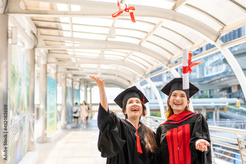 Two Asian women wore graduate gowns are throwing certificates and smiling widely
