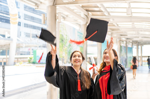 Two Asian women wore graduate gowns are throwing their hats and smiling widely